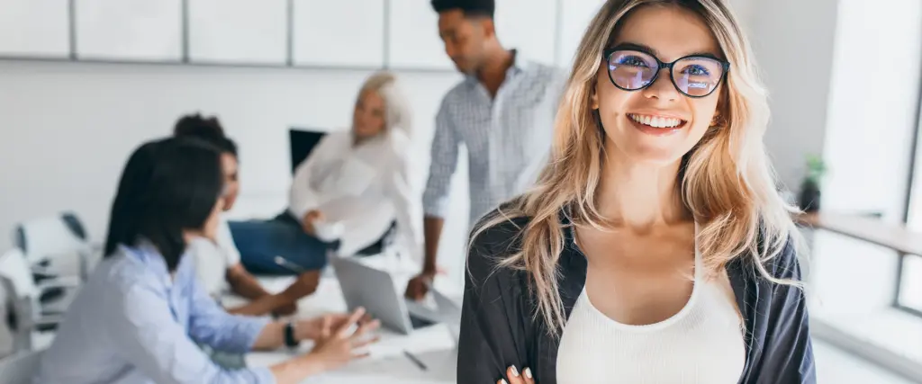 Junge Werkstudentin lächelt im Büro vor Kolleginnen und Kollegen – Symbolbild für Werkstudierendenstelle bei der dbs Delta Business Service GmbH.